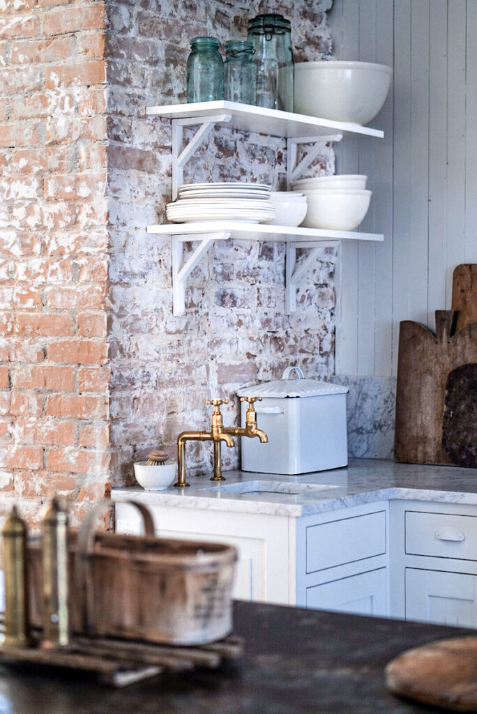 Open shelves that are attached to a brick wall and  full of stoneware and ironstone dishes. 