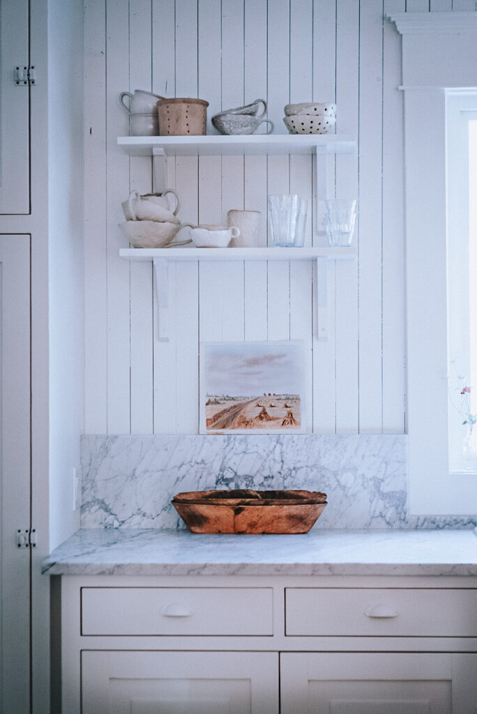 Beautiful hand painted water color painting displayed in a kitchen with open shelves and Carrera marble countertops.