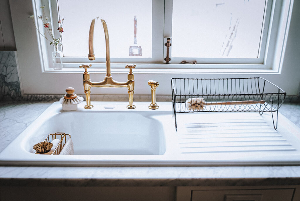 Large farmhouse sink with a drainboard and unlacquered brass faucet with a sprayer from Devol.