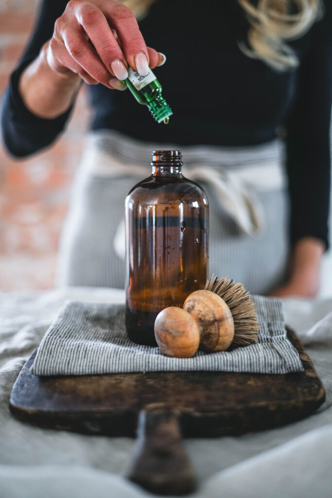 Adding essential oils to homemade all purpose cleaning solution in a glass spray bottle.