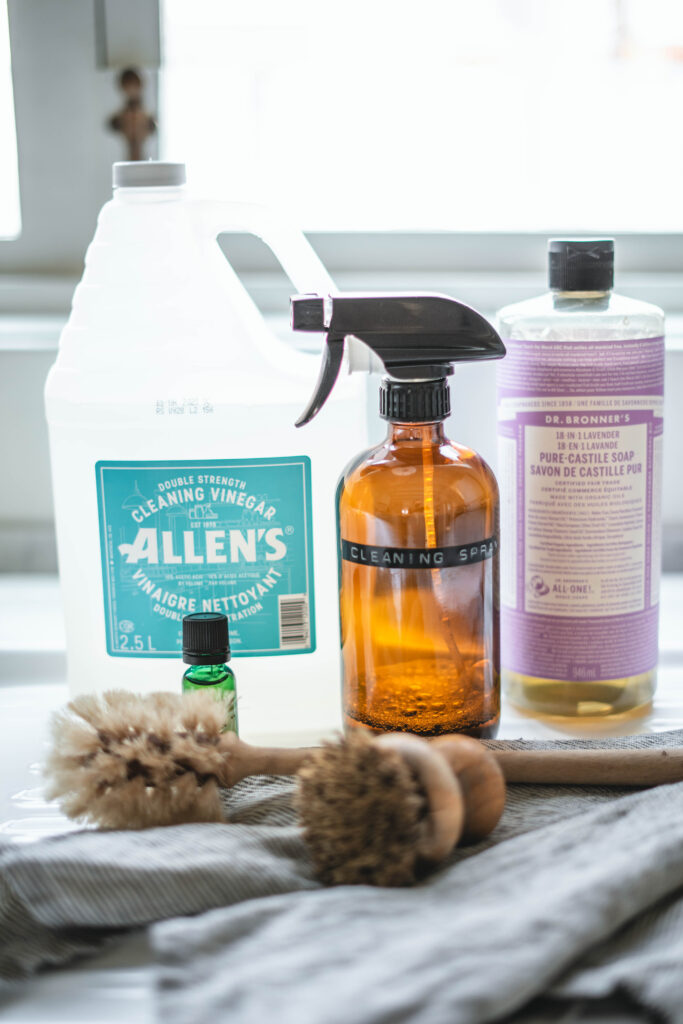 Cleaning vinegar, castile soap, essential oil, and an amber cleaning spray bottle that are all ingredients to make a cleaning solution.