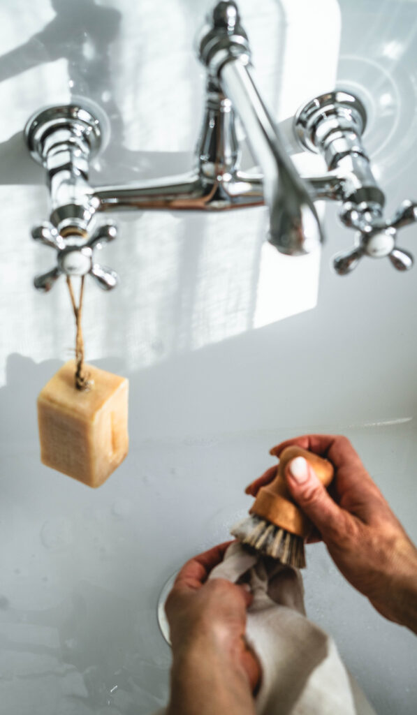 Scrubbing a stain out of a linen towel in a sink using a scrub brush