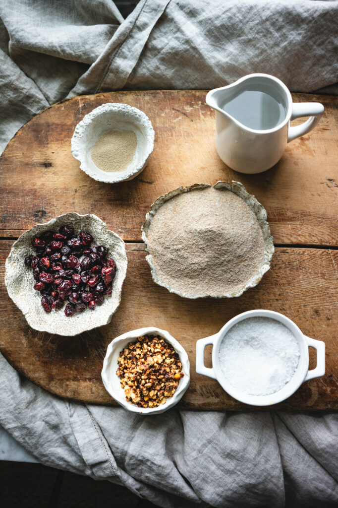 Ingredients for cranberry walnut bread including dried cranberries, toasted walnuts, yeast, salt, and flour.