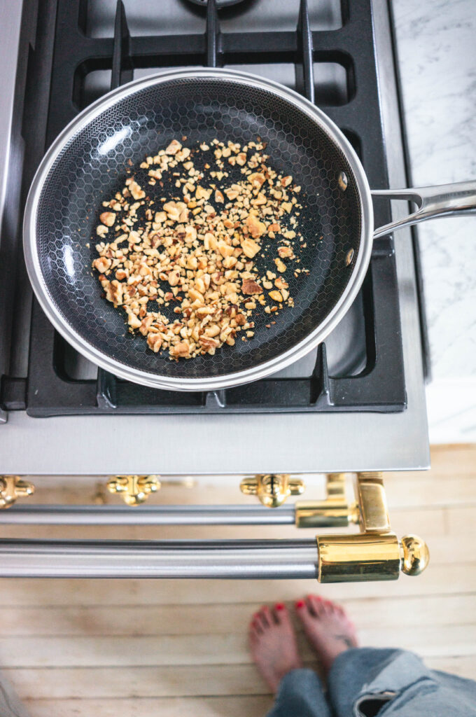 Toasting walnuts in a pan to make cranberry walnut bread.