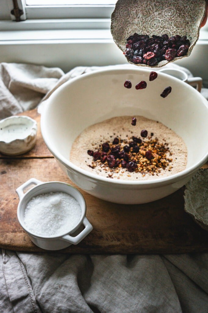 Adding cranberries to a bowl of ingredients to make bread.