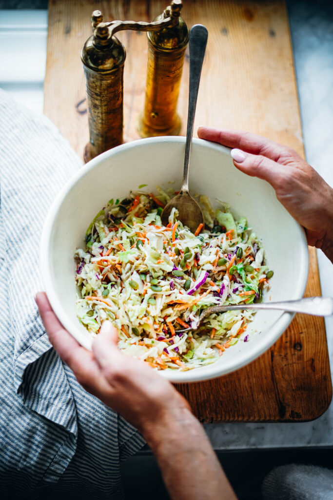 Large bowl of healthy coleslaw that is ready to serve with silver salad tongs.